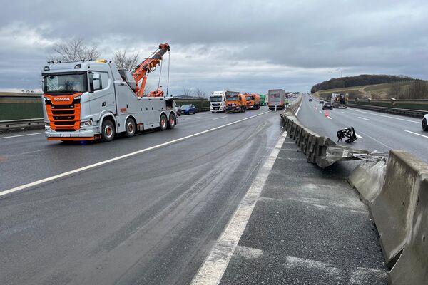 Ein Abschleppwagen hilft auf der Autobahn, wo ein Unfall und eine beschädigte Betonbarriere sichtbar sind. | © Name