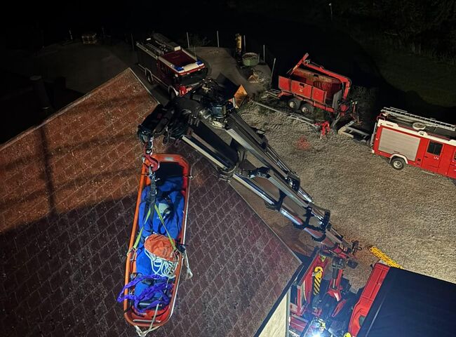 Ein Feuerwehrteam rettet mit einer Drehleiter eine Person von einem Dach bei Nacht, umgeben von Einsatzfahrzeugen.